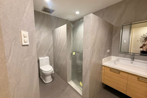 Second bathroom in the Banilad condo with gray stone-look tiles and a glass shower