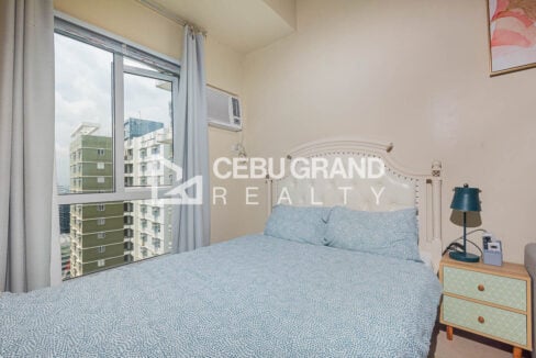 Bed with a tufted headboard and bedside lamp beside a city-view window