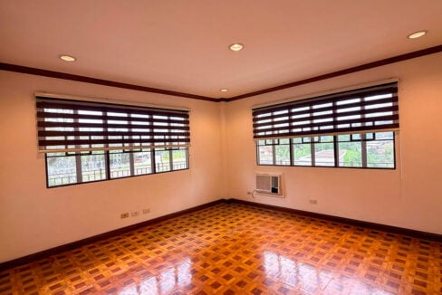 Bedroom with parquet flooring, two windows with blinds and a window-type air conditioner