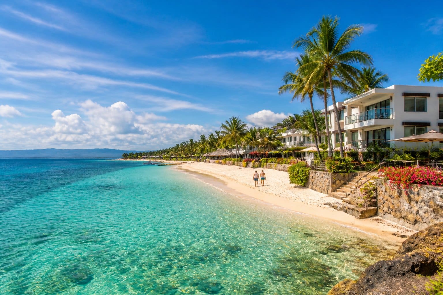 A peaceful beachfront neighborhood with clear turquoise waters, white sand, palm trees, and modern houses along the shore.