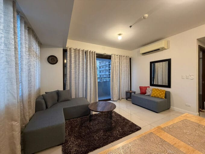 Sectional sofa and accent chair in the living area of 1BR corner condo at The Alcoves