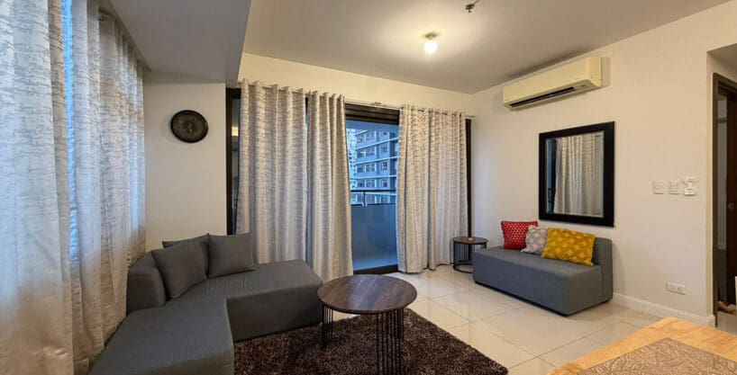 Sectional sofa and accent chair in the living area of 1BR corner condo at The Alcoves
