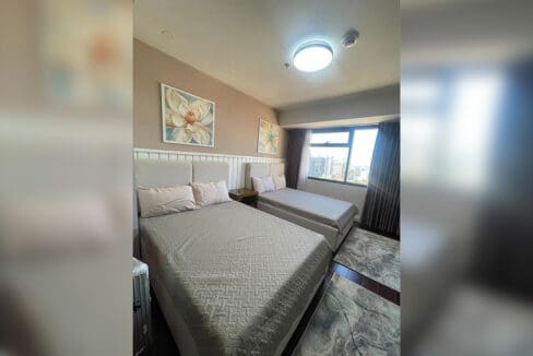 Second bedroom angled view showing twin beds and floor-length curtains at Alcoves 2BR