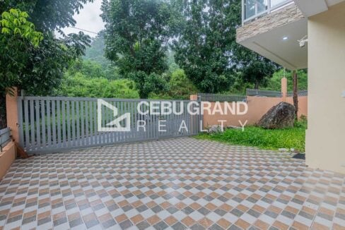 Sliding gate onto the tiled driveway, beside a lawn with boulders