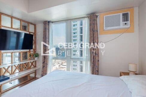 Bed with rattan headboard and bedside lamps against the corner windows at the high-floor studio for rent at Solinea Tower 2