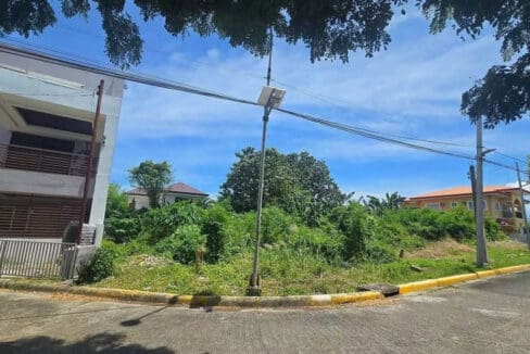 Vacant corner lot on a concreted road with streetlight and built-out homes alongside
