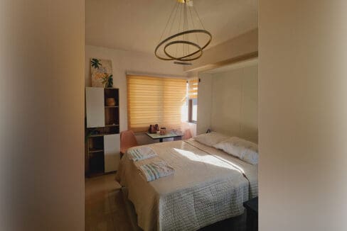 Bed with ring chandelier, zebra blinds and desk area at the furnished studio for sale in Mabolo, Cebu City