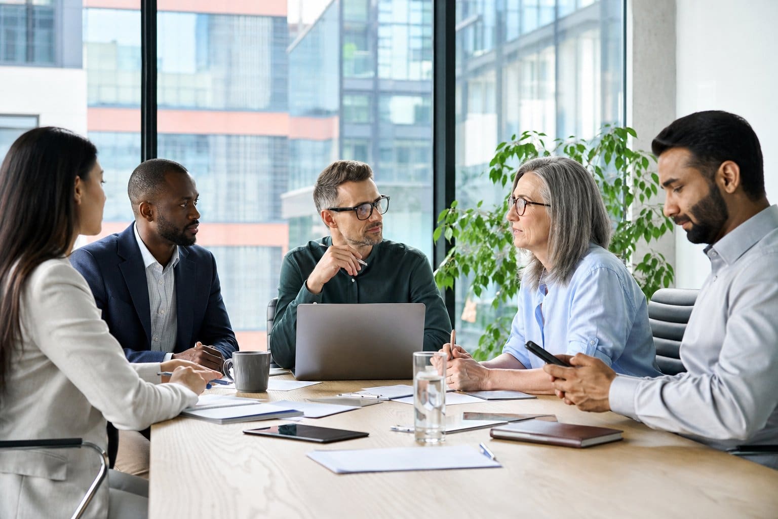A group of business professionals having a focused discussion around a conference table with one person checking a smartphone.