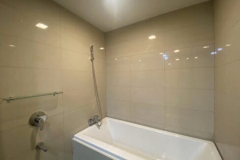 Bathtub with a handshower against pale stone-look wall tiles