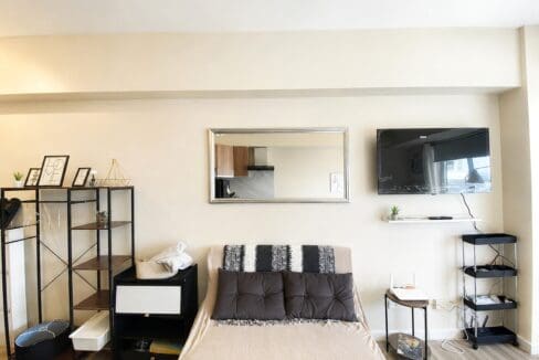 Sofa below a framed mirror and wall-mounted television, beside an open shelving unit