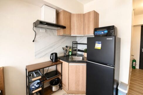Kitchenette in light timber with a black counter, range hood and a refrigerator with a microwave above it