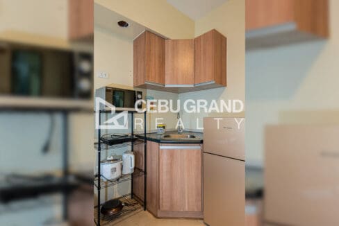 Kitchen corner with timber cabinets, stainless sink, microwave, rice cooker and kettle on a wire shelf