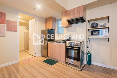 Kitchen with timber cabinets, range hood, gas range with oven and refrigerator, beside the bathroom door