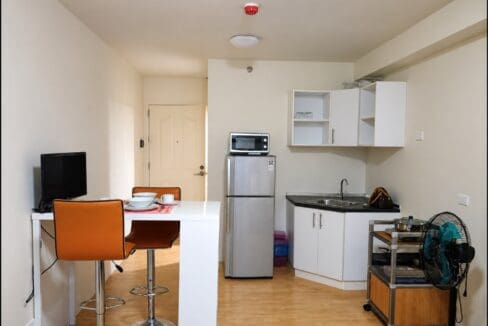 Kitchenette with white cabinets, a refrigerator and microwave, and the breakfast counter beside the entry door