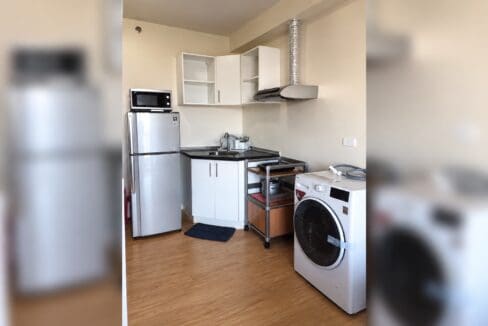 Kitchen corner of this Cebu IT Park studio with a range hood, black counter and a washing machine