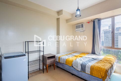 Bed at the window end with a bedside table, washing machine and wire shelving alongside