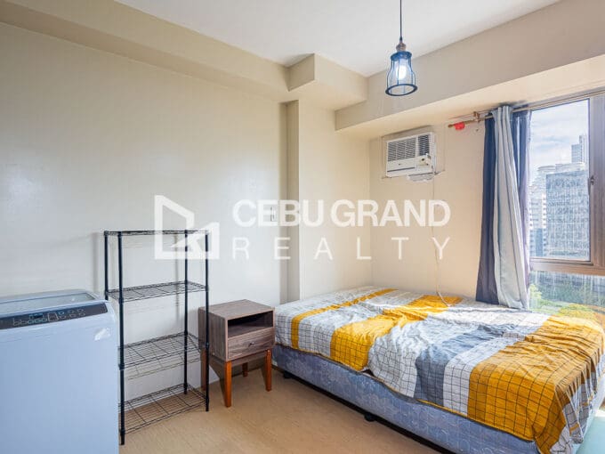 Bed at the window end with a bedside table, washing machine and wire shelving alongside