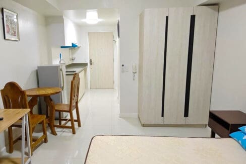 Round timber dining table with two carved chairs, kitchenette and tall wardrobe by the entry