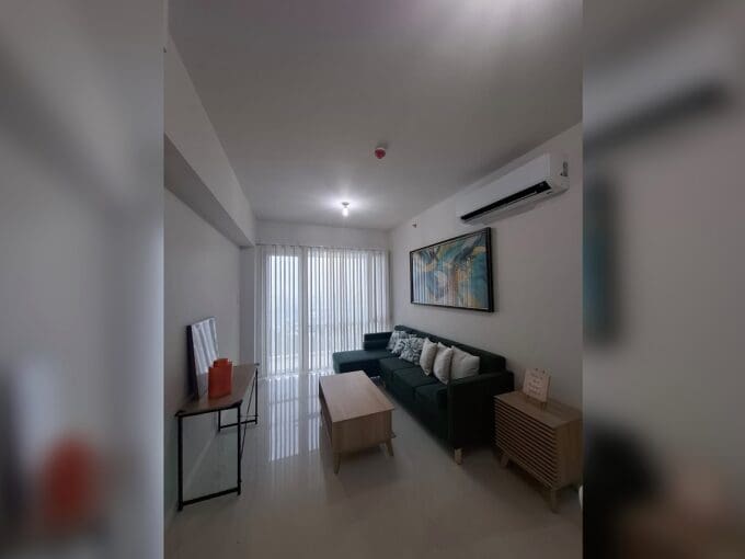Living area with a green L-shaped sofa and gloss floor tiles in a furnished 3BR condo for rent at Marco Polo Residences.