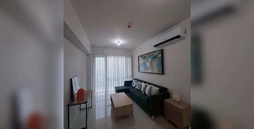 Living area with a green L-shaped sofa and gloss floor tiles in a furnished 3BR condo for rent at Marco Polo Residences.