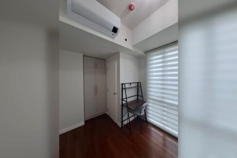 Bedroom with a built-in wardrobe, desk and chair beside a window with zebra blinds.