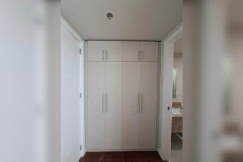 Run of white built-in wardrobes with the bathroom door open beyond.