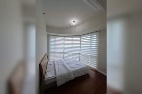 Bedroom with a bed set into a curved bay window dressed in zebra blinds.