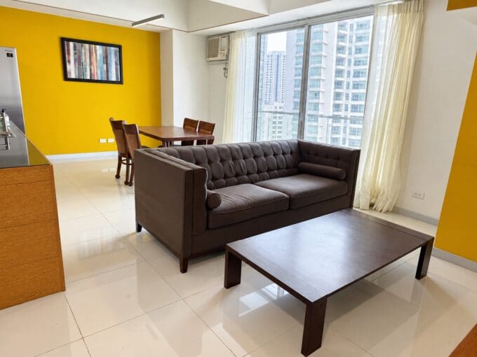 Living area with a brown tufted leather sofa and timber coffee table beside floor-to-ceiling windows at Marco Polo Residences Lahug