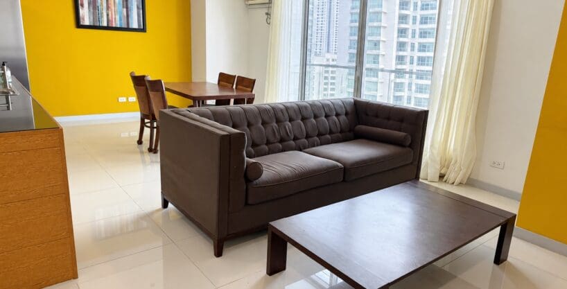 Living area with a brown tufted leather sofa and timber coffee table beside floor-to-ceiling windows at Marco Polo Residences Lahug