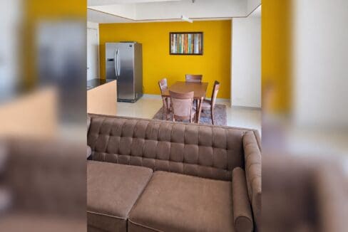 View across the tufted sofa to the dining area and stainless refrigerator in the open living space