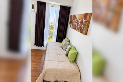 Second bedroom with a beige daybed, green cushions and dark curtains at the window