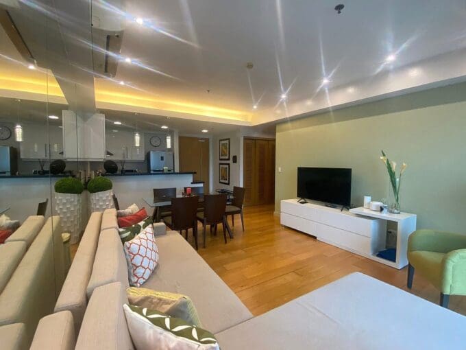 Open living and dining area with wood plank floors and a mirrored feature wall in a furnished 1BR condo for rent at Park Point Residences.