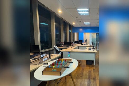 Open-plan desk layout along the window wall of the 15th-floor unit, with the glass-partitioned room and blue accent wall at the rear