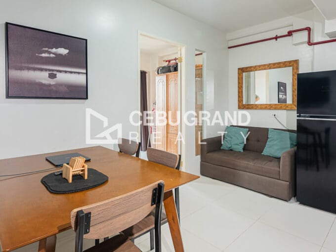 Furnished 1BR condo for rent at Royal Oceancrest Mactan, with a four-seater dining table, tufted sofa and refrigerator