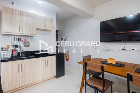 Kitchen counter with light timber cabinets beside the dining table and wall-mounted television