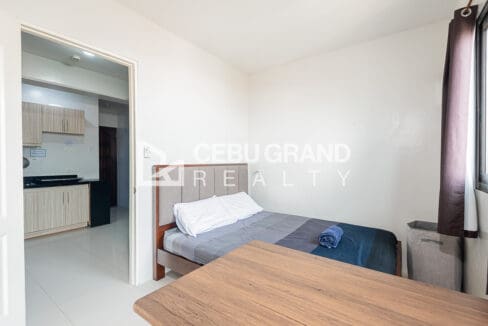 Double bed with an upholstered headboard, the kitchen seen through the bedroom doorway