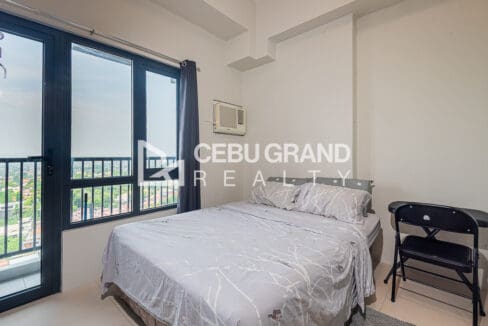 Sleeping area with a double bed, window-type air conditioner, folding desk and balcony door