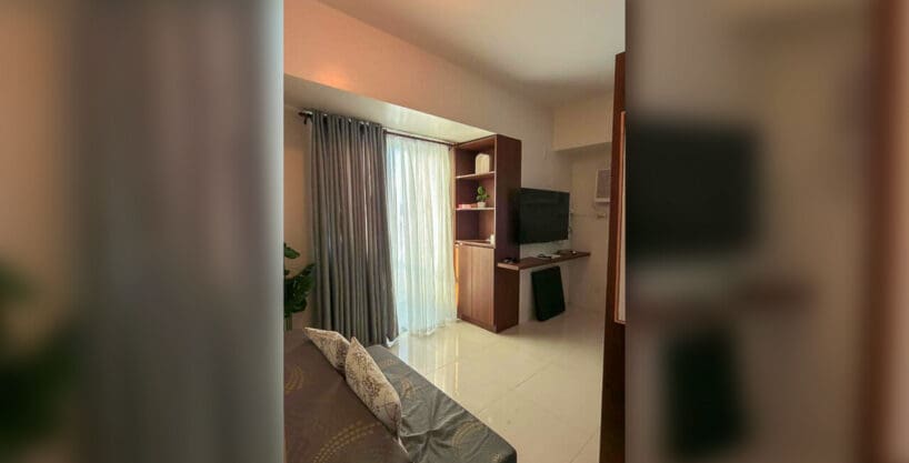 Living area with sofa, built-in shelving and wall-mounted TV in a furnished studio for rent at Taft East Gate, Mabolo