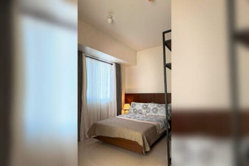 Double bed with timber headboard panel and bedside lamp in a furnished studio