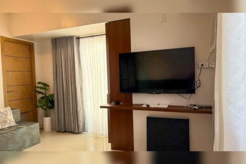 Wall-mounted TV on a floating timber shelf beside the balcony curtains