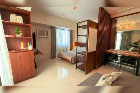 Open-plan studio with bed zone behind open shelving, dining counter and built-in cabinets at Taft East Gate, Cebu City