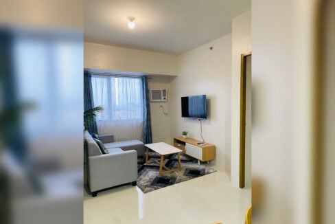 Living room with an L-shaped sofa, wall-mounted TV and window-type air conditioning