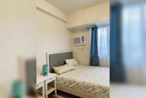 Bed with a tufted headboard, bedside table and window-type air conditioning