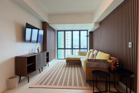 Living area with mustard L-shaped sectional, timber slat feature wall, and city views in the 2BR condo for rent at 38 Park Avenue