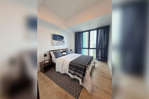 Second bedroom with timber headboard and navy curtains overlooking the city in the 2BR condo for rent at 38 Park Avenue