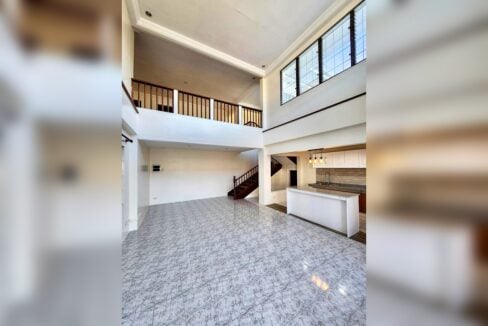 Double-height living room with high windows and a view of the kitchen