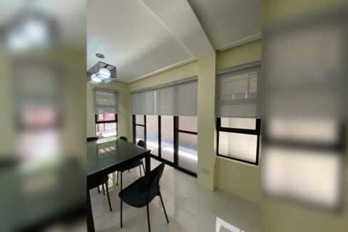 Glass-top dining table beside sliding glass doors with roller blinds
