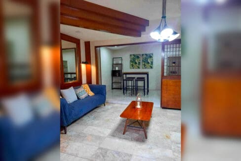 Living area with blue sofa, timber coffee table, wall mirror and exposed timber ceiling beams