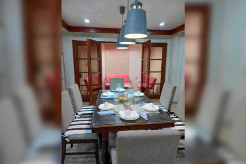 Dining table set for six under pendant lights, with glass-paned doors to a sitting room