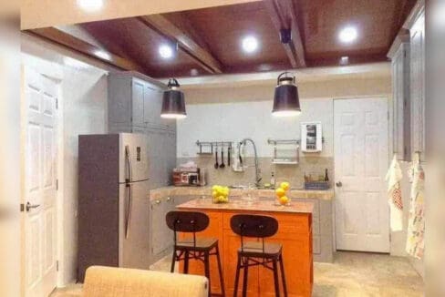 Kitchen with grey cabinets, refrigerator and an island counter with two bar stools